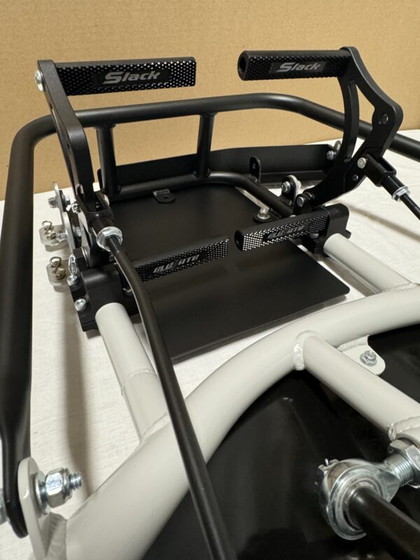 Close-up of a Foot Pan - For Elevate, Pursuit & Xpect CHAMP KART racing simulator pedal set with metal bars and mechanisms on a white surface in front of a beige background.