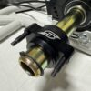 Close-up of the Foot Pan - For Elevate, Pursuit & Xpect CHAMP KART featuring a metal shaft, black housing with a logo, and bolts securing it to other metal parts.