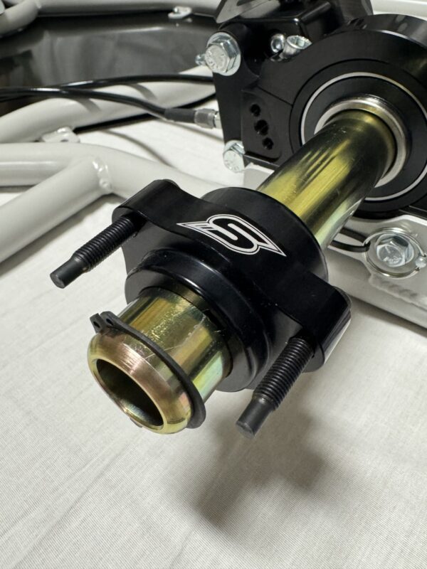 Close-up of the Foot Pan - For Elevate, Pursuit & Xpect CHAMP KART featuring a metal shaft, black housing with a logo, and bolts securing it to other metal parts.