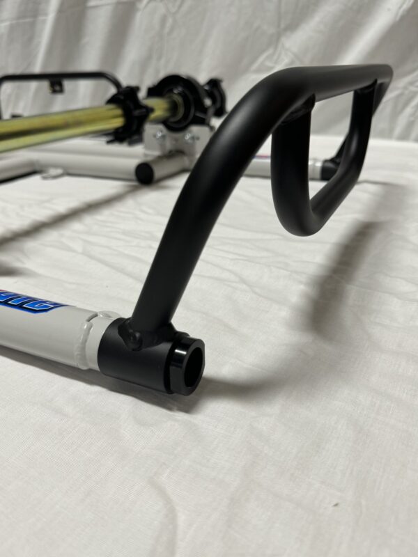 A close-up view of the Foot Pan for Elevate, Pursuit & Xpect CHAMP KART with a focus on the black handle and part of the white and yellow frame. The background is a plain white fabric.