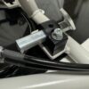 Close-up view of the Foot Pan - For Elevate, Pursuit & Xpect CHAMP KART featuring a metal mechanism with a clamp, bolts, and a cable attached to a grey frame.