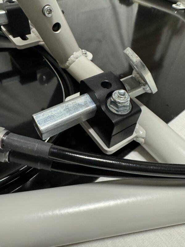 Close-up view of the Foot Pan - For Elevate, Pursuit & Xpect CHAMP KART featuring a metal mechanism with a clamp, bolts, and a cable attached to a grey frame.