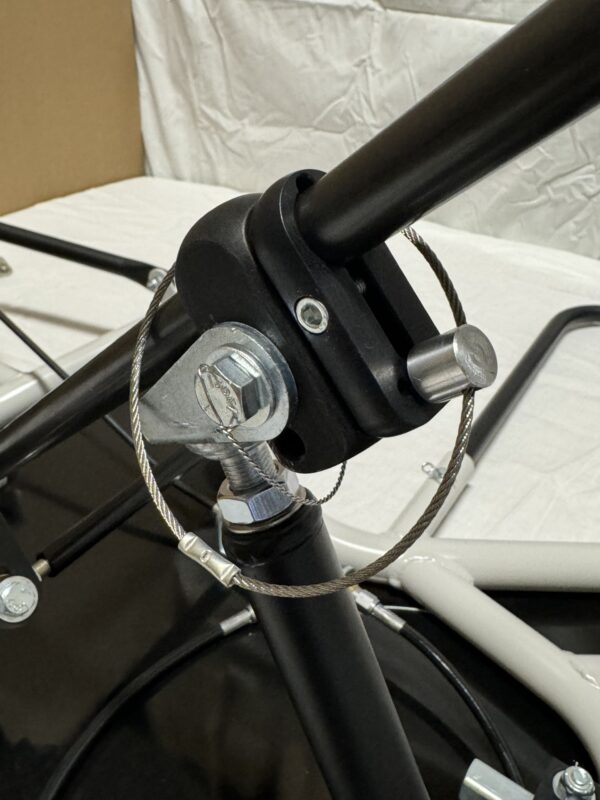 Close-up of the metal hardware on a black pole, showcasing the bolted attachment with a securing cable and pin on the Foot Pan for Elevate, Pursuit & Xpect CHAMP KART.