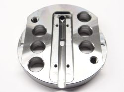 Close-up of a circular metal component with multiple round holes and a central groove against a white background.