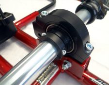 Close-up of a mechanical component, showing a metal rod secured by black and red mounting brackets with bolted connections.