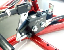 Close-up of a mechanical component with black and red parts, including a metal bracket, hydraulic connections, and a pump with logos.