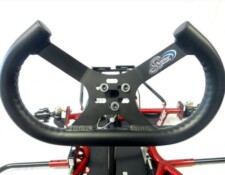 Close-up image of a black racing go-kart steering wheel with visible mounting hardware and red chassis components in the background.