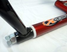 Close-up of a red metallic frame with a logo reading "XPEST" and black tubular structures connected by a white ring and a silver bolt at the joint.