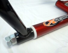 Close-up of a red metallic frame with a logo reading "XPEST" and black tubular structures connected by a white ring and a silver bolt at the joint.