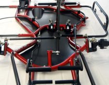 A close-up view of the underside of a red and black go-kart chassis showing various components including the frame, steering rods, and mounts.