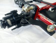Close-up image of a mechanical assembly with black and red components, featuring a spherical joint and various bolts and fasteners. The surface is flat and appears to be resting on a white background.