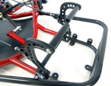 Close-up image of a pedal mechanism on a go-kart, featuring black pedal arms with circular cutouts, a red frame, and various connecting components.