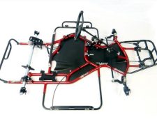 A red and black go-kart frame with a steering wheel, seat base, and visible components such as axles and brackets, displayed on a white background.